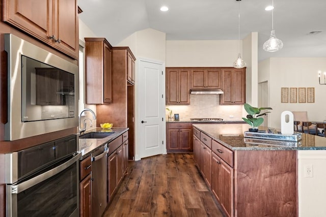 kitchen with dark wood-style flooring, a kitchen island, a sink, appliances with stainless steel finishes, and dark stone countertops