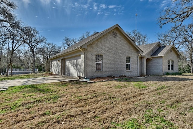 view of side of home with driveway, a lawn, an attached garage, fence, and brick siding