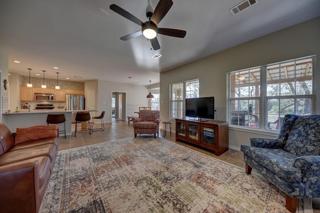 living area with light tile patterned floors, ceiling fan, visible vents, and baseboards