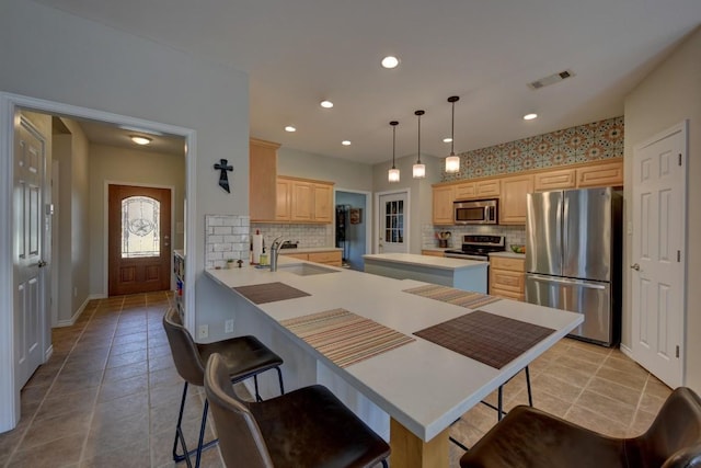 kitchen featuring a breakfast bar area, light brown cabinets, a sink, visible vents, and appliances with stainless steel finishes