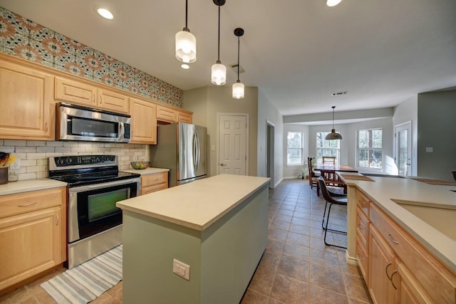 kitchen with tasteful backsplash, light countertops, appliances with stainless steel finishes, light brown cabinets, and a kitchen island