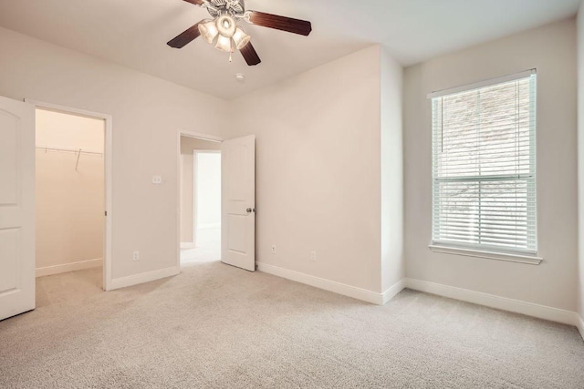 unfurnished bedroom with a ceiling fan, a walk in closet, light colored carpet, and baseboards