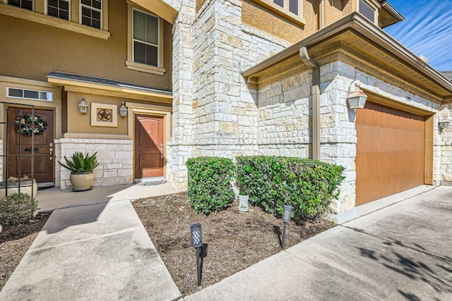 entrance to property with a garage, stone siding, and stucco siding