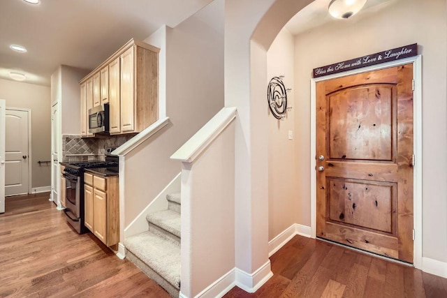 foyer entrance featuring arched walkways, stairway, wood finished floors, and baseboards