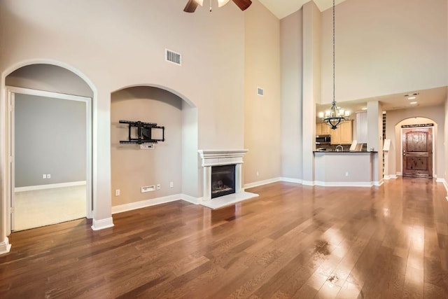 unfurnished living room featuring baseboards, visible vents, a fireplace with raised hearth, dark wood-style flooring, and ceiling fan with notable chandelier