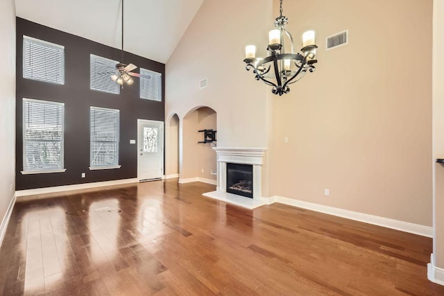 unfurnished living room with arched walkways, ceiling fan with notable chandelier, wood finished floors, visible vents, and a glass covered fireplace