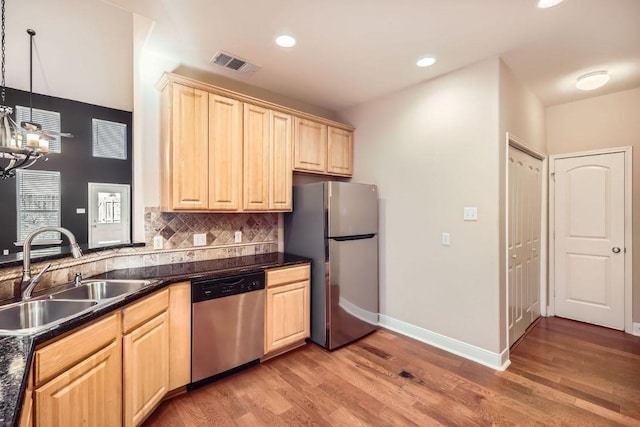 kitchen featuring dark countertops, light brown cabinets, appliances with stainless steel finishes, and a sink