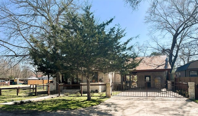 view of front facade featuring stone siding, decorative driveway, a fenced front yard, and a gate