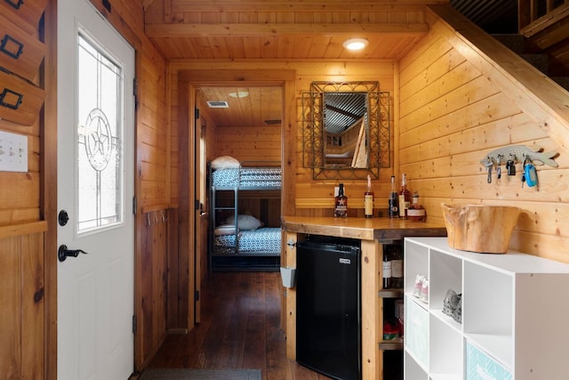 bar featuring plenty of natural light, wooden ceiling, dark wood-type flooring, refrigerator, and wood walls