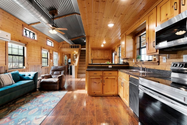 kitchen with appliances with stainless steel finishes, open floor plan, a sink, and wood walls