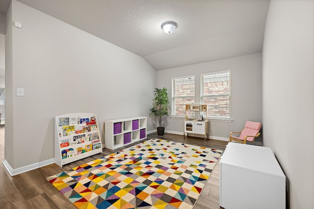 game room with a textured ceiling, baseboards, vaulted ceiling, and wood finished floors