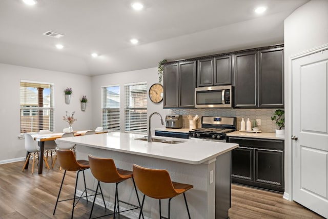 kitchen featuring a breakfast bar, a sink, light countertops, appliances with stainless steel finishes, and decorative backsplash