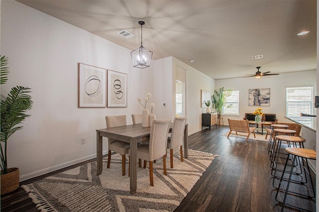 dining room with ceiling fan with notable chandelier, dark wood finished floors, visible vents, and baseboards