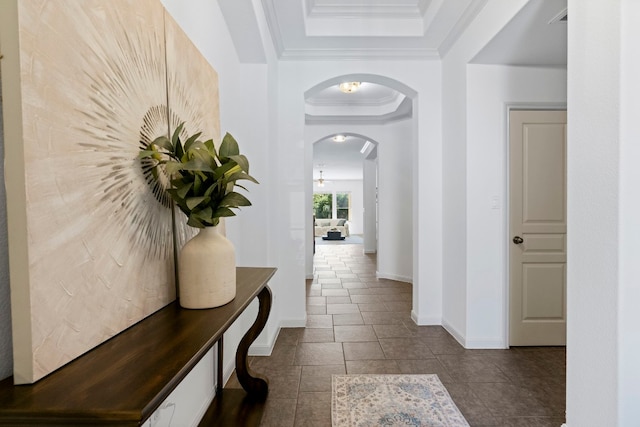 corridor featuring arched walkways, a tray ceiling, ornamental molding, and baseboards