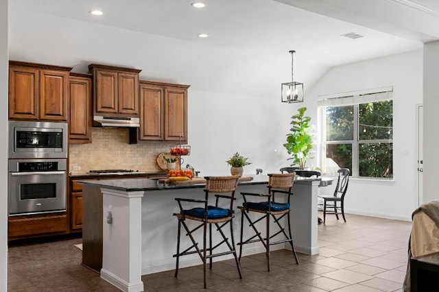 kitchen with visible vents, decorative backsplash, appliances with stainless steel finishes, a kitchen breakfast bar, and under cabinet range hood