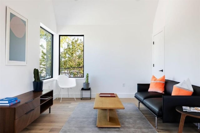 living area featuring vaulted ceiling, light wood-type flooring, and baseboards