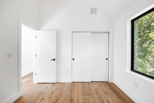 unfurnished bedroom featuring light wood-style floors, multiple windows, baseboards, and a closet