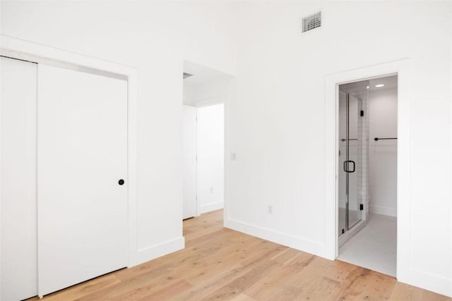 unfurnished bedroom with ensuite bathroom, a closet, visible vents, and light wood-style floors