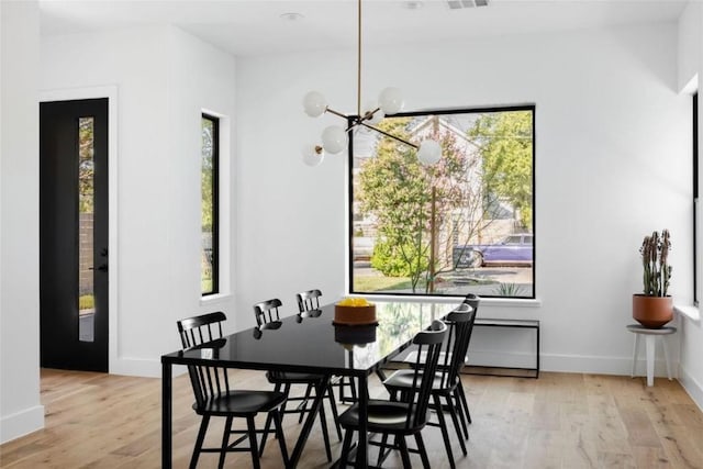 dining area with light wood-type flooring, baseboards, visible vents, and a notable chandelier