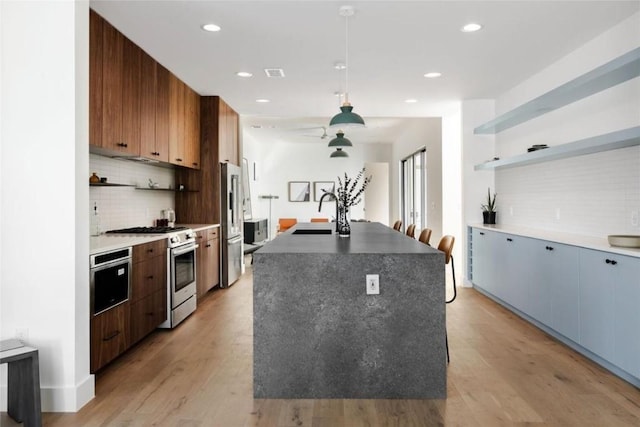 kitchen with a kitchen island with sink, light wood-style flooring, stainless steel appliances, a sink, and open shelves