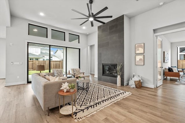 living area with recessed lighting, a tiled fireplace, light wood-style flooring, and baseboards