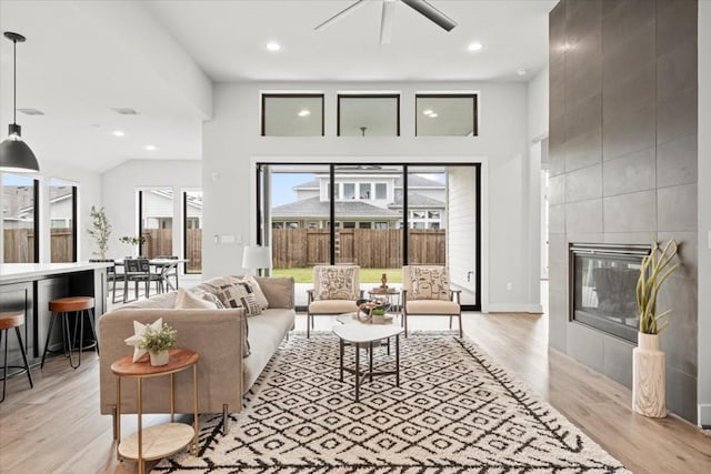 living area featuring light wood-type flooring, a ceiling fan, a wealth of natural light, and a tile fireplace