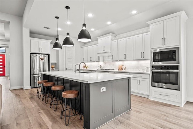 kitchen featuring stainless steel appliances, a breakfast bar, a sink, light wood-style floors, and tasteful backsplash