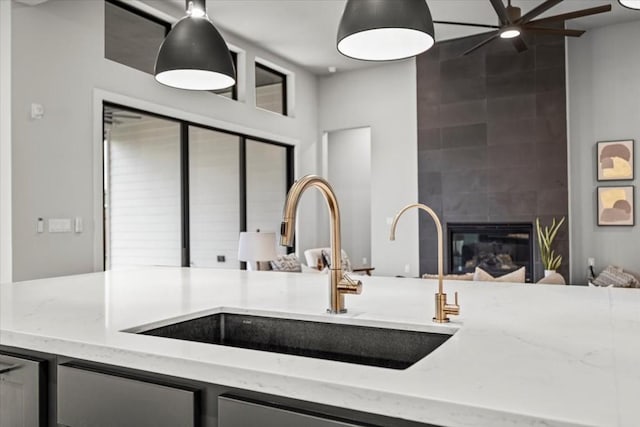 kitchen featuring a tile fireplace, open floor plan, decorative light fixtures, light stone countertops, and a sink