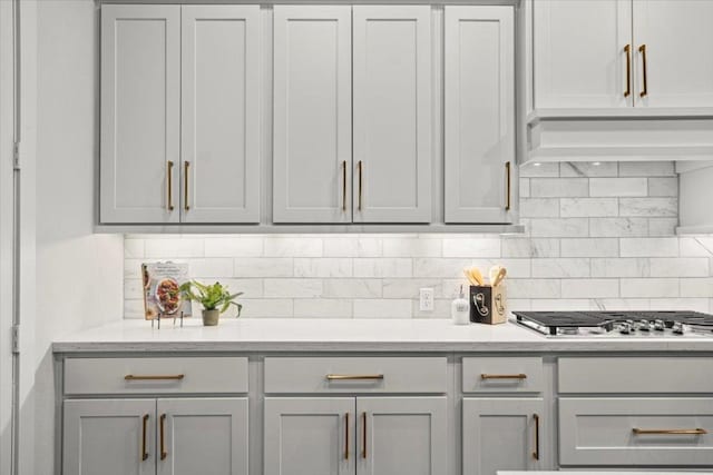 kitchen featuring light stone countertops, custom exhaust hood, gray cabinets, stainless steel gas stovetop, and backsplash