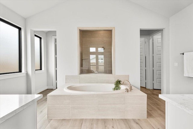 full bathroom featuring a garden tub, vaulted ceiling, vanity, and wood finished floors