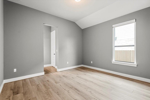 spare room with baseboards, vaulted ceiling, and wood finished floors