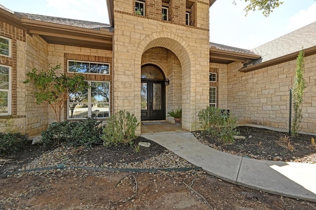 view of exterior entry with a shingled roof, french doors, and stone siding