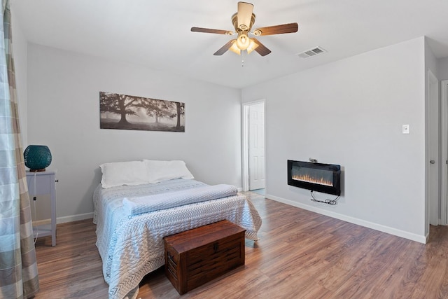 bedroom with a glass covered fireplace, visible vents, wood finished floors, baseboards, and heating unit