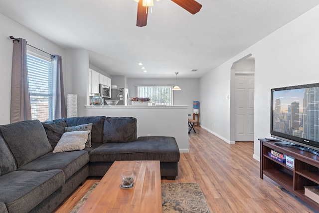 living room featuring light wood-style flooring, baseboards, and ceiling fan