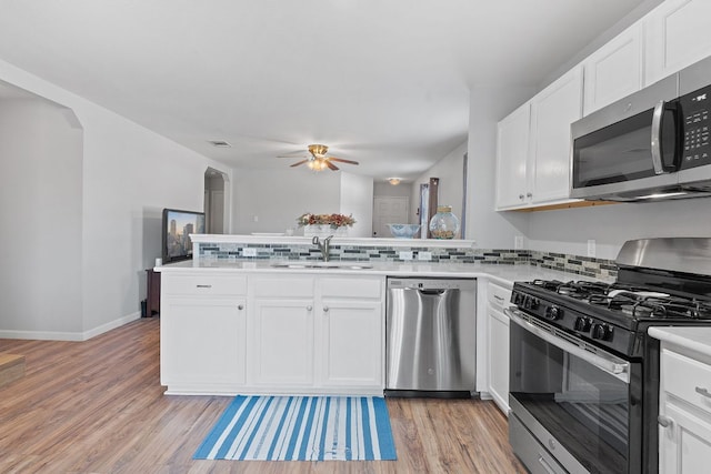 kitchen featuring light wood-style floors, a peninsula, appliances with stainless steel finishes, a sink, and decorative backsplash