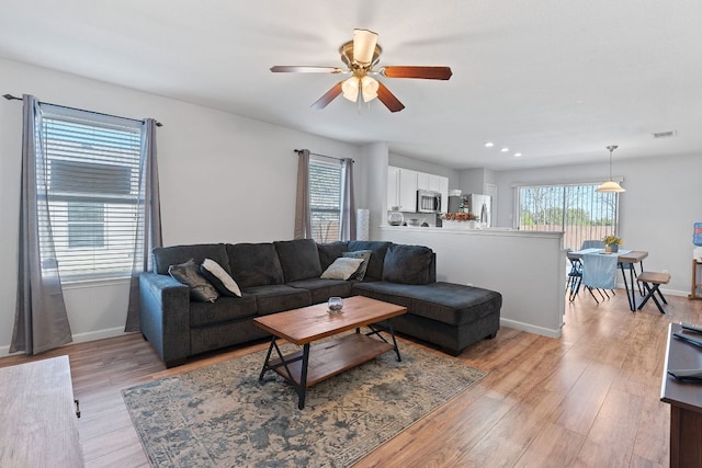 living room featuring visible vents, light wood-style flooring, a ceiling fan, and baseboards