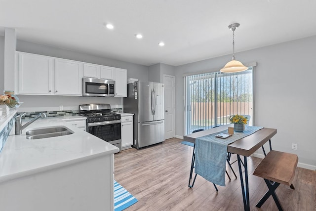 kitchen featuring stainless steel appliances, a sink, white cabinetry, light wood-style floors, and pendant lighting