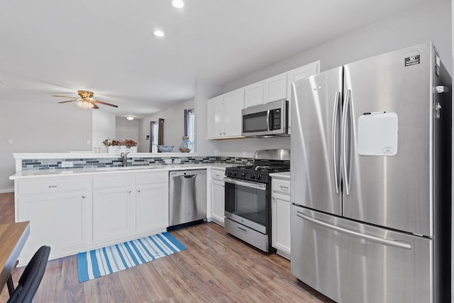 kitchen featuring stainless steel appliances, a peninsula, a sink, white cabinets, and light wood finished floors