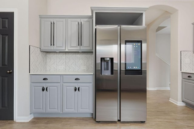 kitchen with arched walkways, stainless steel fridge with ice dispenser, gray cabinets, light wood-style floors, and baseboards