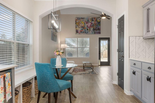 dining space with arched walkways, ceiling fan with notable chandelier, plenty of natural light, and light wood-style flooring