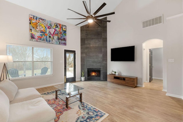 living area featuring arched walkways, a tile fireplace, a high ceiling, wood finished floors, and visible vents