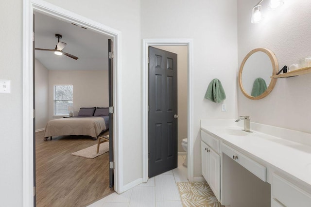 ensuite bathroom with toilet, wood finished floors, vanity, baseboards, and a ceiling fan