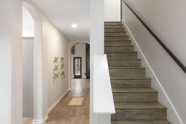 stairs featuring arched walkways, baseboards, wood finished floors, and recessed lighting