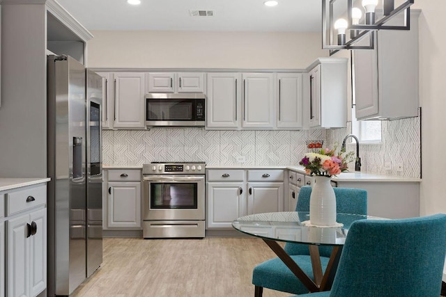 kitchen featuring stainless steel appliances, visible vents, light wood-style floors, light countertops, and tasteful backsplash