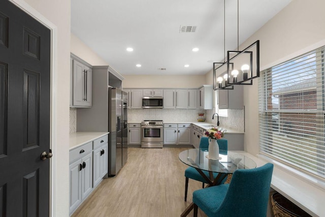 kitchen featuring tasteful backsplash, appliances with stainless steel finishes, gray cabinets, light countertops, and light wood-style floors