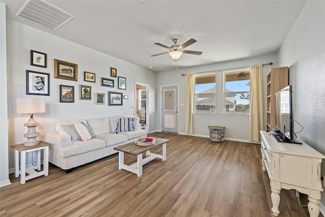 living area with baseboards, ceiling fan, visible vents, and wood finished floors