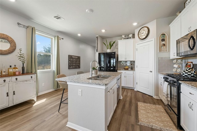 kitchen featuring a center island with sink, visible vents, light wood-style flooring, a sink, and black appliances