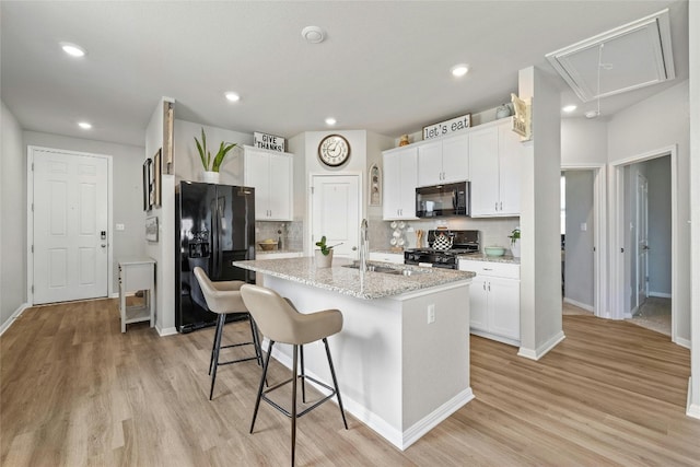 kitchen featuring white cabinetry, a sink, black appliances, light wood-type flooring, and a kitchen breakfast bar