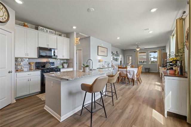 kitchen featuring white cabinets, light wood-type flooring, backsplash, black appliances, and an island with sink