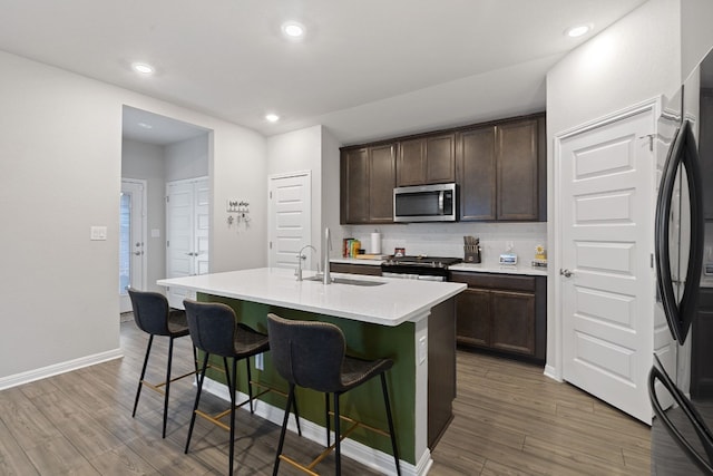 kitchen with appliances with stainless steel finishes, wood finished floors, dark brown cabinetry, and a kitchen breakfast bar